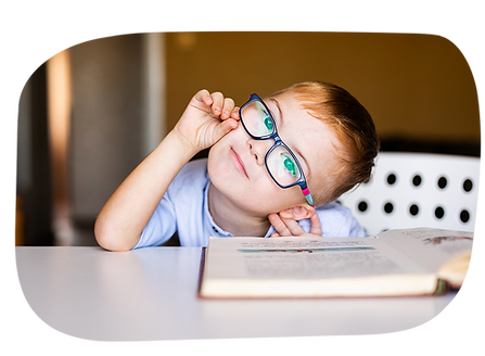 A cute kindergarten-age Caucasian boy with a learning difference  adjusts his glasses while he reads a book